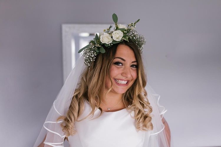 Beaming bride to be wearing muted green flower crown with veil and white dress