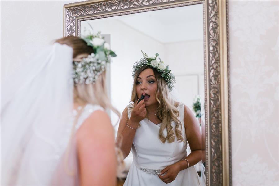 Bride to be applies Illamasqua lipstick in a large mirror wearing a white wedding dress