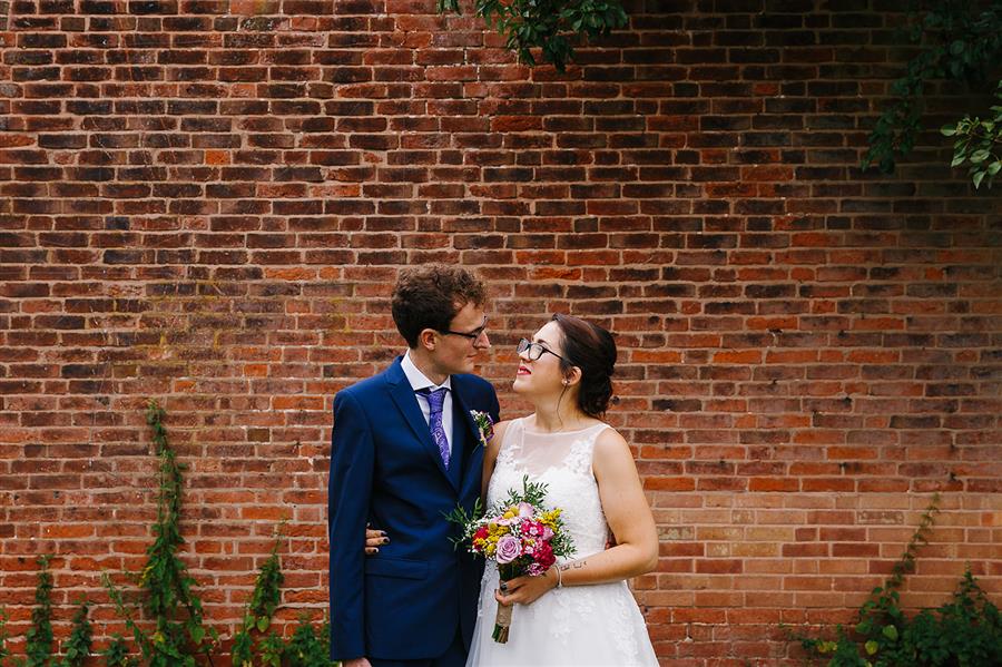 Bride and groom in front of red brick garden wall
