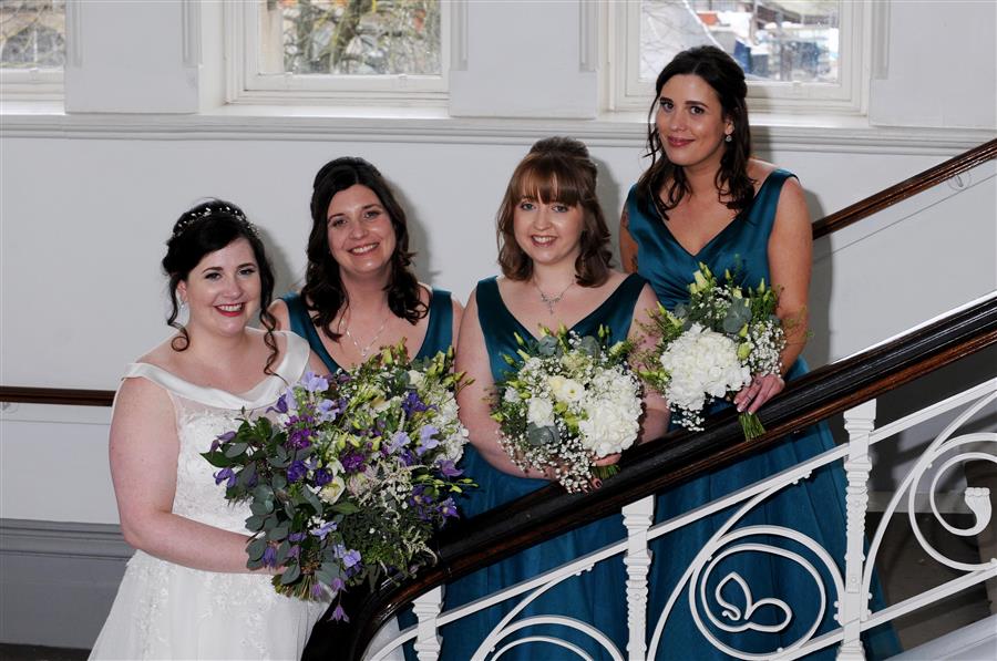 A smiling bride and three bridesmaids in teal with bouquets