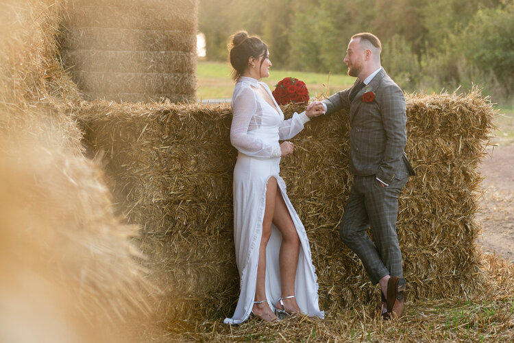 Barn wedding couple next to a hay bale with red rose bouquet and thigh split wedding dress