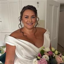 Tanned brunette bride with face framed hair smiles at camera with off the shoulder white dress