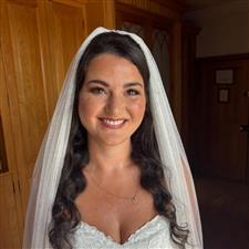 Tanned bride with white veil and dress, smiles at the camera