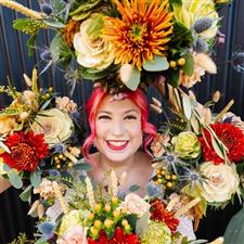 Pink haired bride smiles at the camera surrounded by her bouquets. She has pink hair, pink lipstick and silver gems on her face