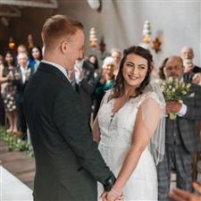 Brunette bride smiling at registrar holding her husbands hands as they wait to hear 