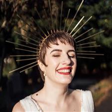 Bride with short hair and gold head piece that looks like the sun smiles as she faces the sunshine wearing red lipstick and a soft gold smoky eye