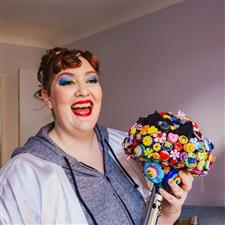 Red haired bride with red lipstick and rainbow eyeshadow laughs past the camera while holding her button bouquet