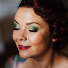 Green and gold smoky eye makeup on dark red haired vintage styled bride with bright red lipstick