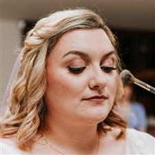 Bride looks down as she has powder applied, showing rose gold eyeshadow