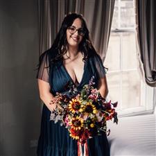Smiling bride with long dark hair smiles at camera wearing a blue dress and holding bouquet with gold star tiara