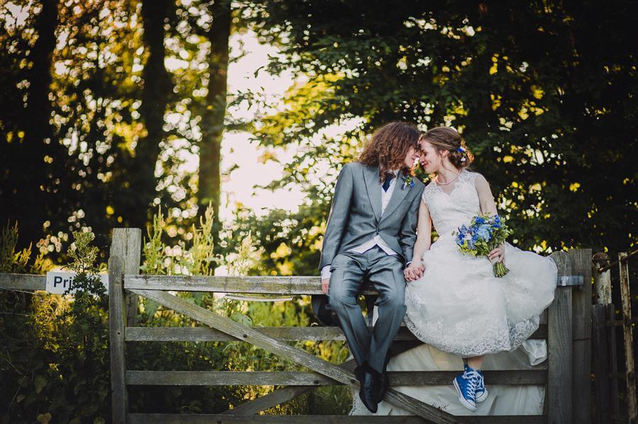 Bride and groom pose on a field gate with their foreheads together