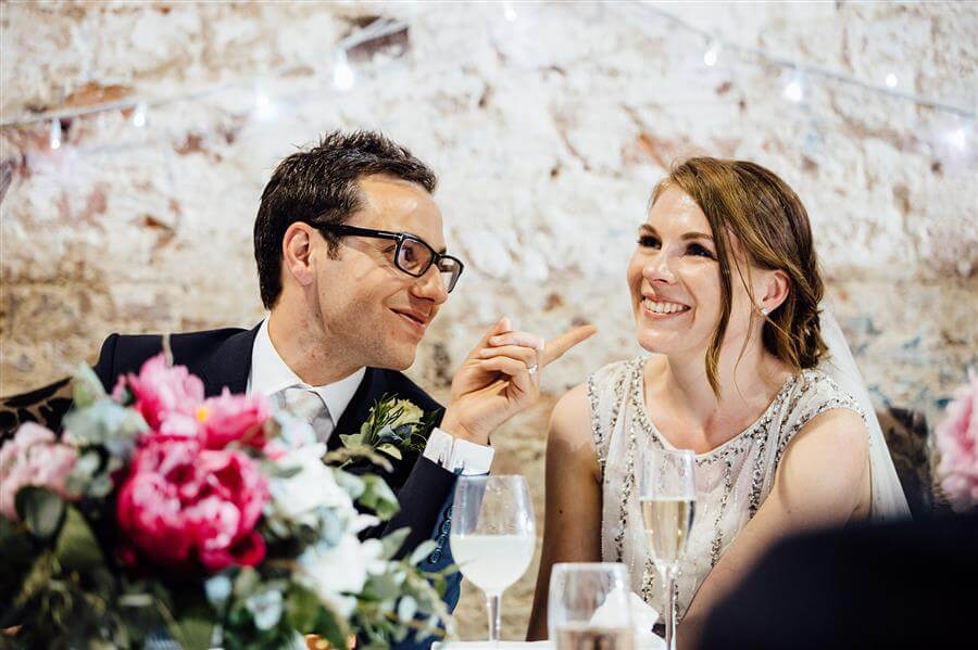 Smiling bride with groom pointing at her, by Humpston and Bull Photography