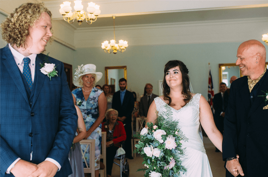 Bride holding a large bouquet wearing white loving looks at husband