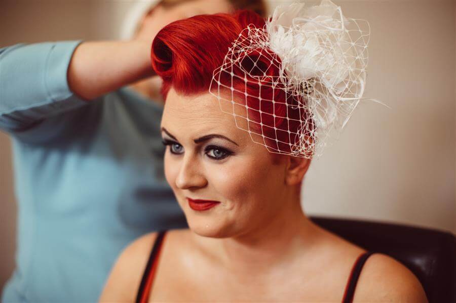 Bride with bright red hair and white birdcage veil has her hair done