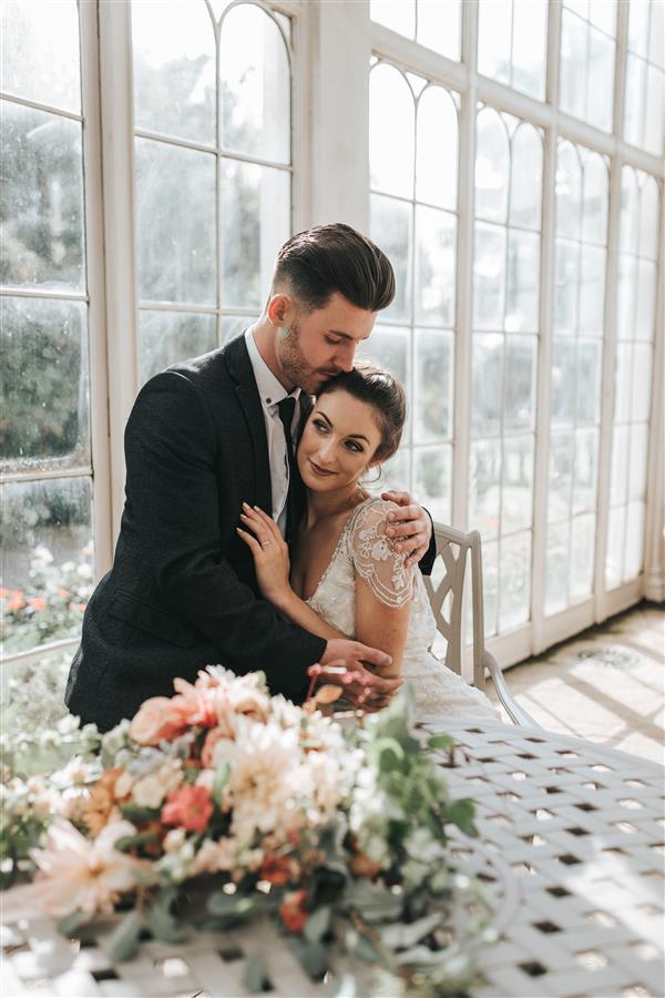 Bride and groom photoshoot in front of large windows with bride wearing white