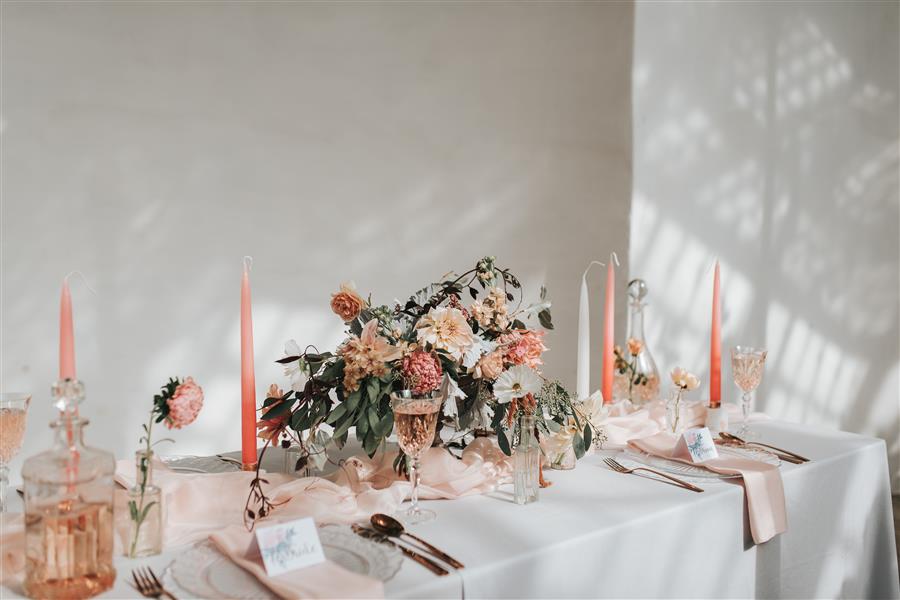 Table with white tablecloth and wedding place settings with pink candles and elaborate floral centre piece