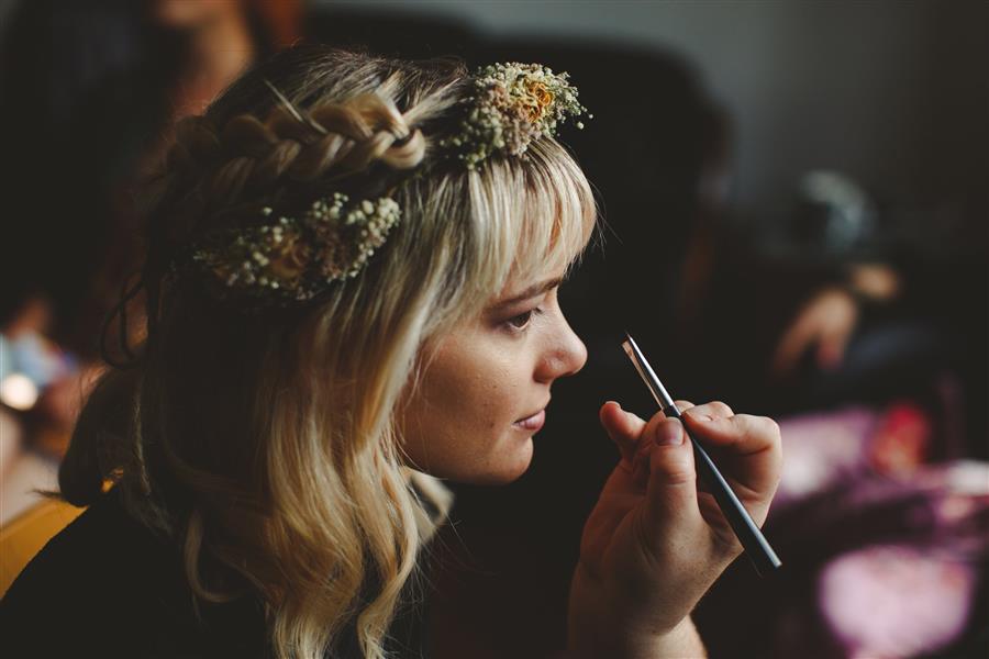 Blonde woman with flower crown watching eyeliner brush