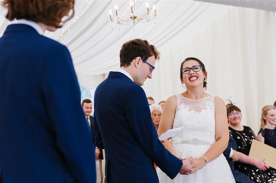 Smiling bride listening to groom make wedding vows by Emily & Katy Photography