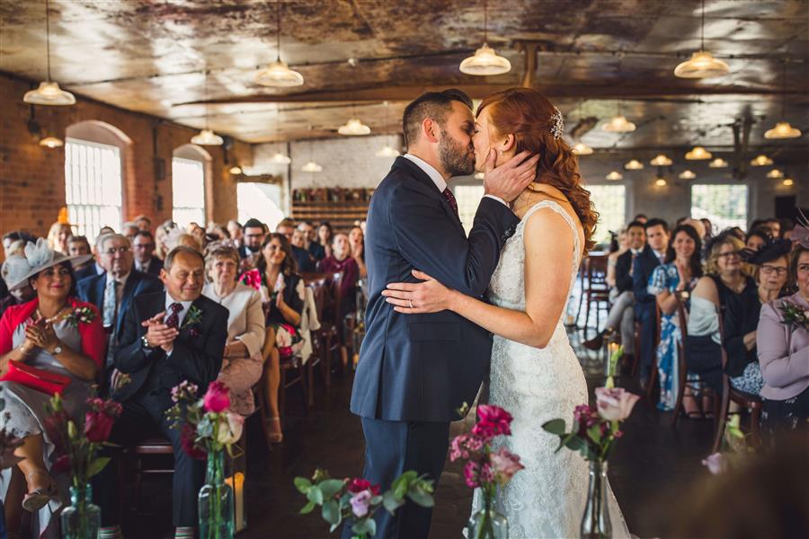 Bride and groom kiss in wedding ceremony in front of guests