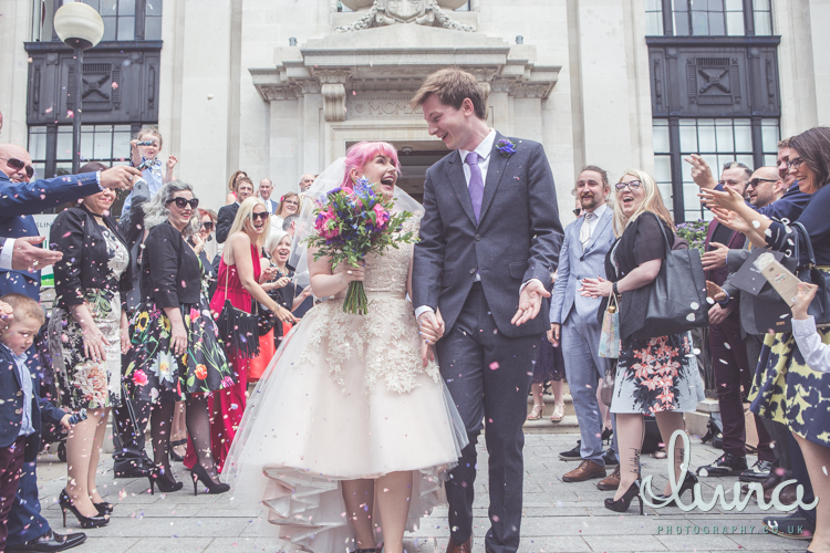 Confetti shot of bride and groom with bride holding large pink bouquet wearing a white dress with pink hair