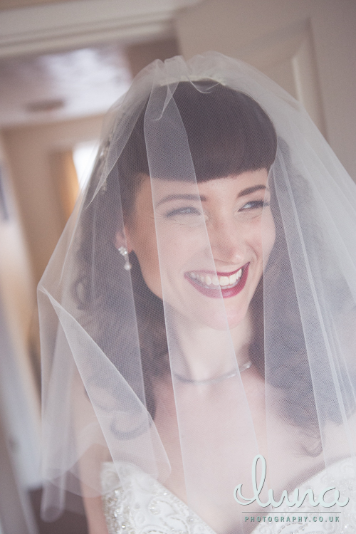 Smiling bride with red lipstick wears white veil over her face